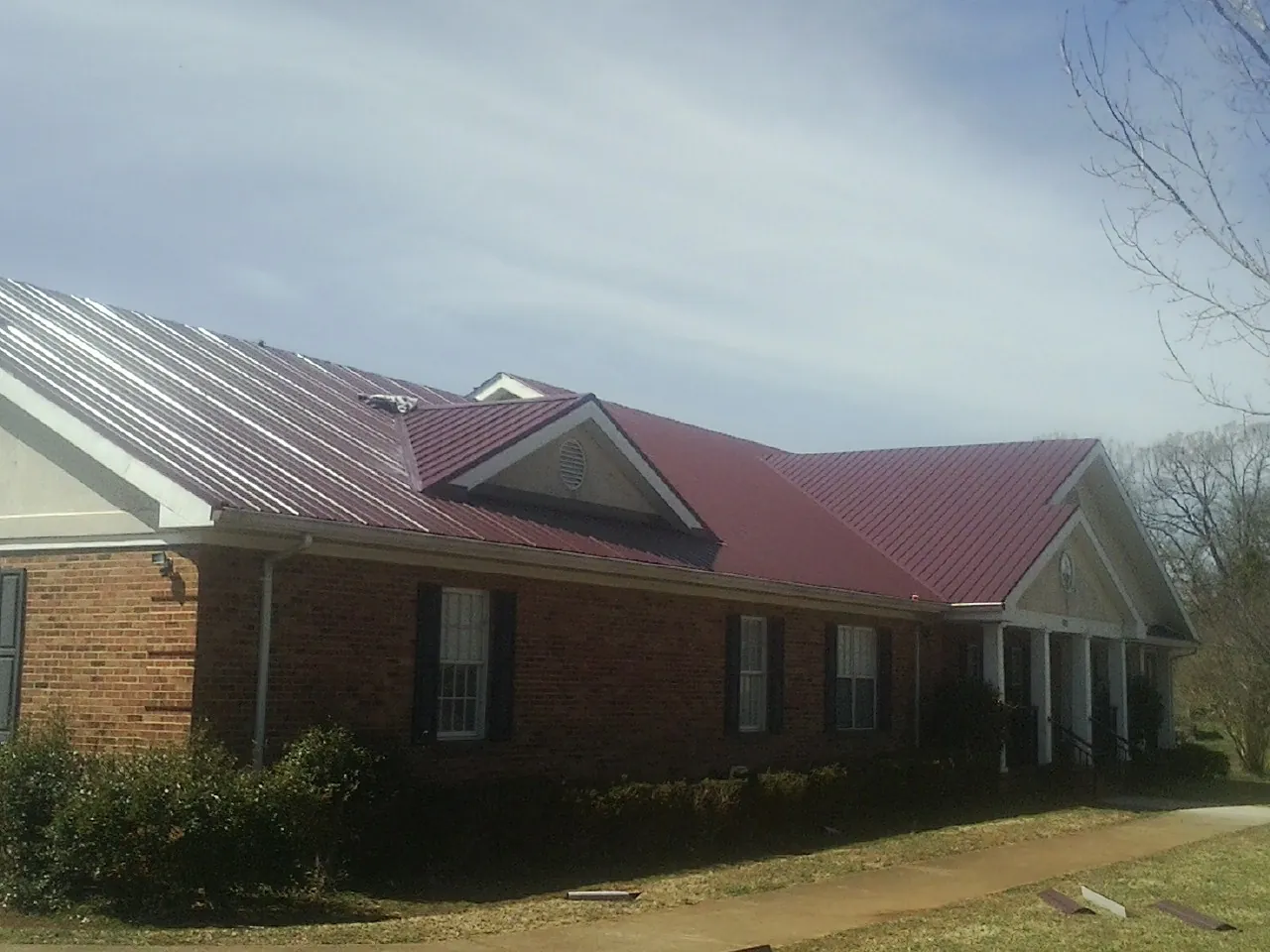 Red metal roof with gabled entries on a long brick building, from a Hail Damage Roof Repair job in Beech Grove